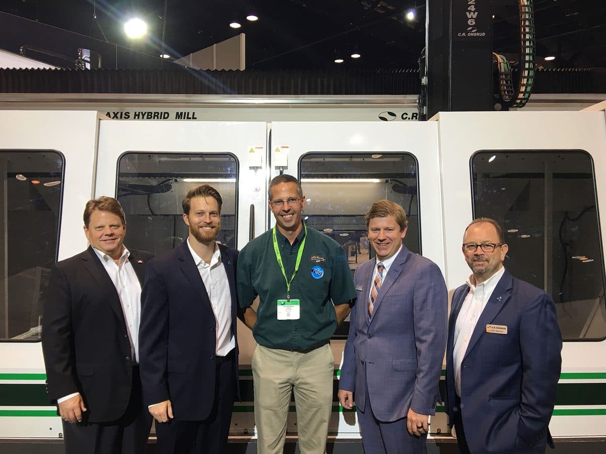 James and colleagues in suits in front of a 5-axis hybrid mill at a trade show