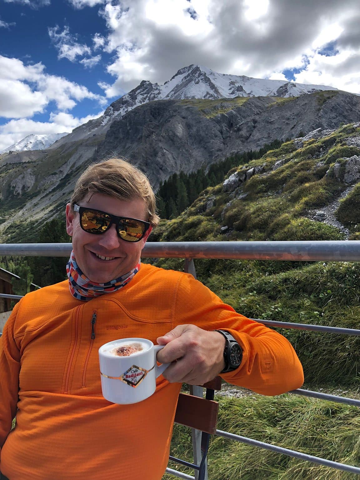 James smiling with a mug of coffee in front of a mountain landscape
