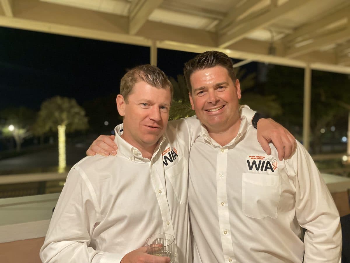 James and a friend in matching WIA shirts, arms around each other at an evening event