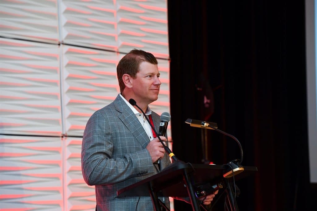 James speaking at the podium during an industry conference
