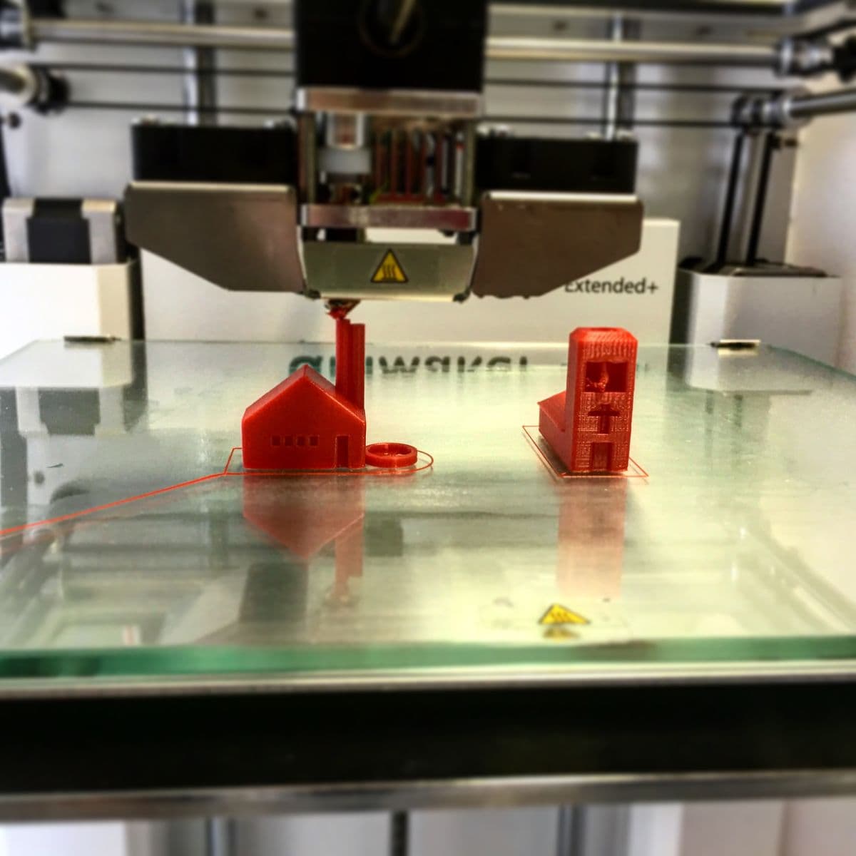 3D printer mid-print building a red plastic part