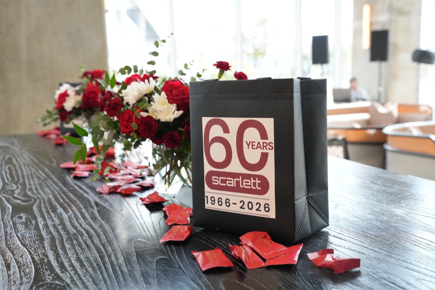 A Scarlett 60 years gift bag beside red and white flowers at the cocktail hour